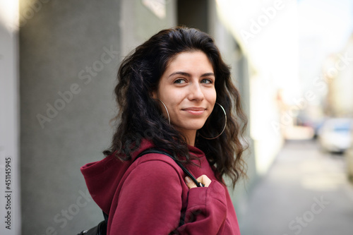 Portrait of young woman standing outdoors on street in city.