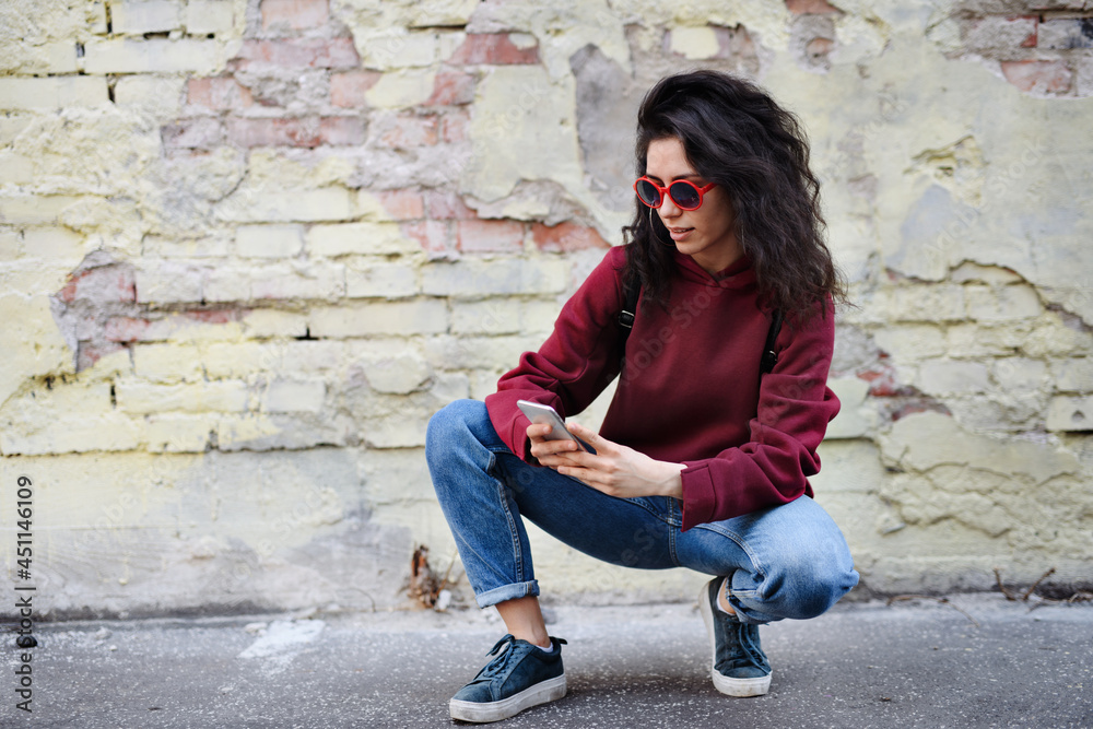 Portrait of young woman standing outdoors on street in city, using smartphone.