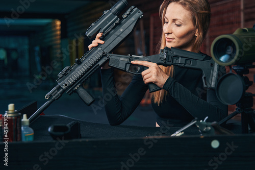 Young woman concentrated on disassembling the assault rifle