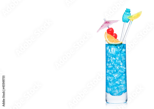 Blue lagoon cocktail highball glass with stirrers and orange slice with sweet cherry and umbrella on white. Vodka and blue curacao liqueur mix.