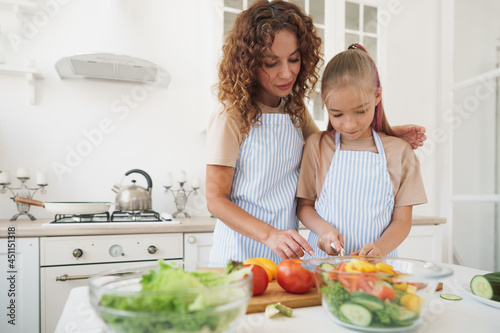 Mommy teaching her teen daughter to cook vegetable salad in kitchen