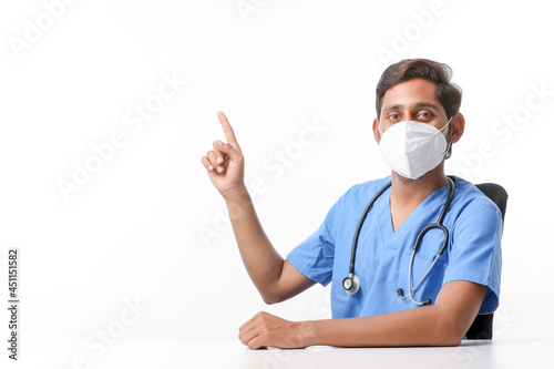 Young indian male doctor wearing mask and pointing with hand at clinic.