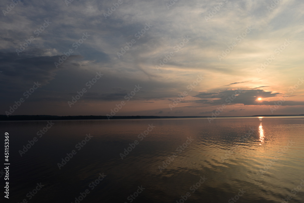 Sunbeam from clouds at sunset over calm lake water
