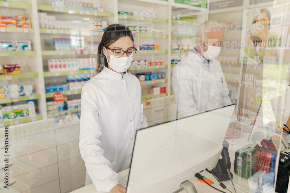 Obraz premium Portrait of a pharmacist and corona virus. An elderly male pharmacist and an adult female apothecary stand behind the counter in a drugstore and sell medicines. They wear uniforms and face masks