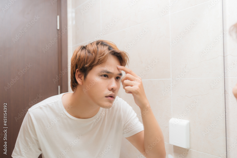 Man looking in mirror and checking his skin in bathroom Man looking in mirror and checking his skin in bathroom