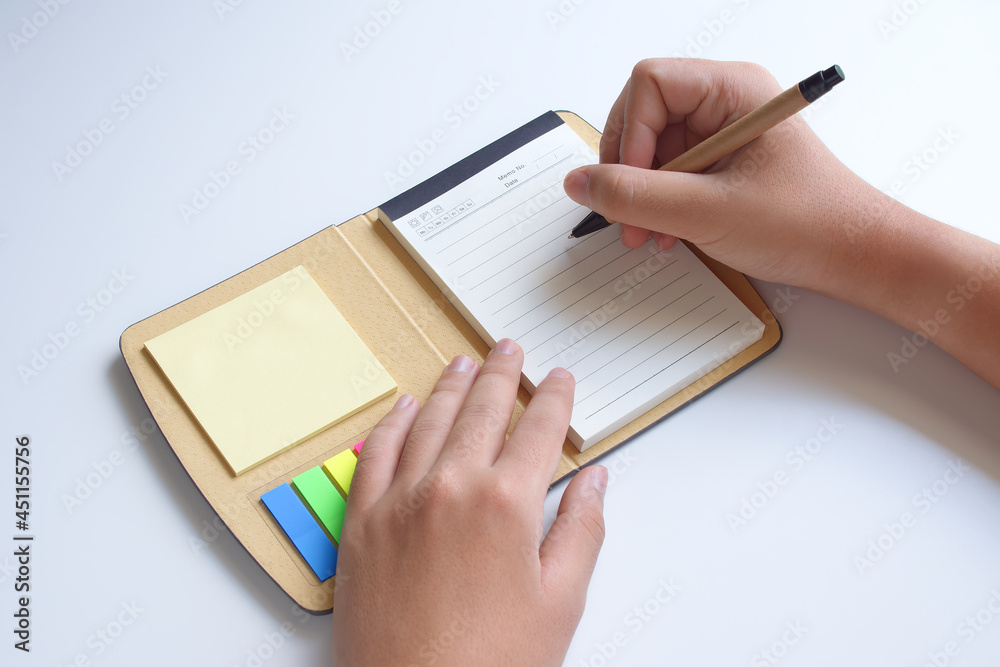 Notebook portable with sticky pad, Hands holding a pen is write for record of income and expenses, Isolated on white background, Pocket book for Organizer planner, Business management lecture memo. Notebook portable with sticky pad, Hands holding a pen is write for record of income and expenses, Isolated on white background, Pocket book for Organizer planner, Business management lecture memo.