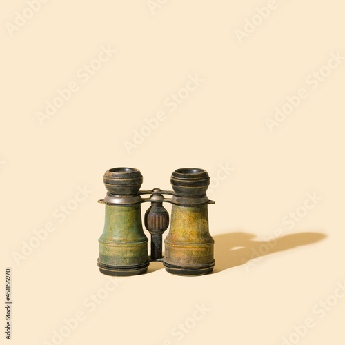 An old authentique antique metal binoculars on beige background with sunny shadow.