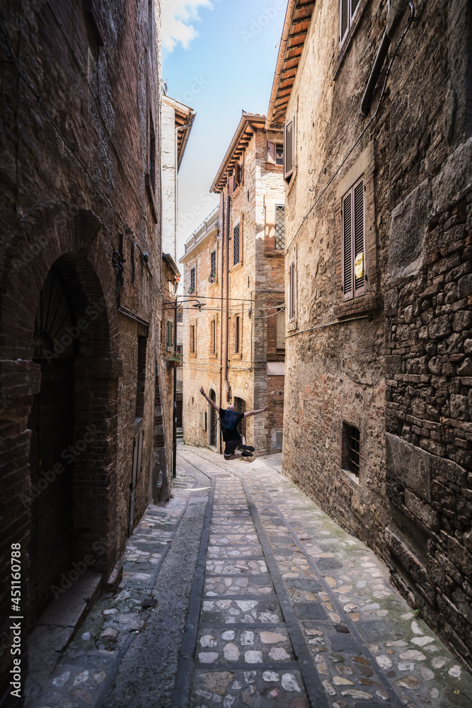 A young man is jumping and having fun in a narrow street in Todi