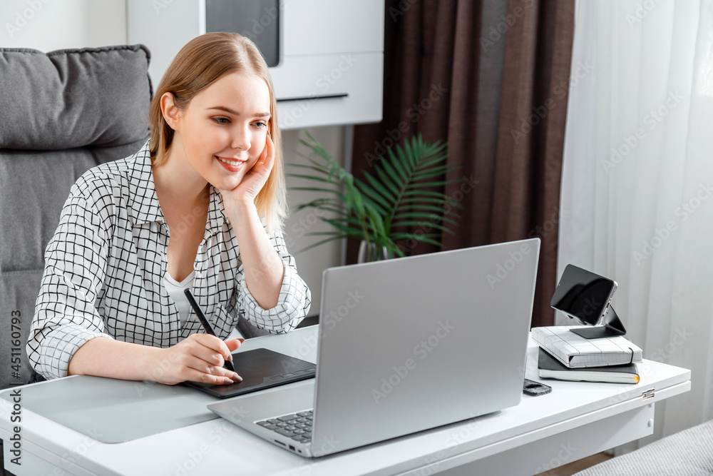Smiling happy Woman designer using graphic tablet and laptop for work in home office. Freelance retoucher illustrator young caucasian blonde woman working remotely from home workspace. Smiling happy Woman designer using graphic tablet and laptop for work in home office. Freelance retoucher illustrator young caucasian blonde woman working remotely from home workspace.