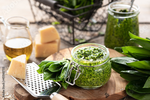 Wild leek pesto with olive oil and parmesan cheese in a glass jar on a wooden table. Useful properties of ramson. Leaves of fresh ramson.