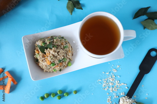Breakfast with oatmeal and green peas, carrot in bowl and tea in cup. Blue background. Top view 