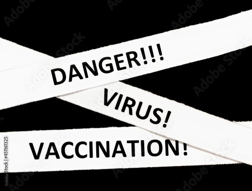 The words " Danger!", " Virus!", "Vaccination!" on scraps of paper on a black background. White security tape