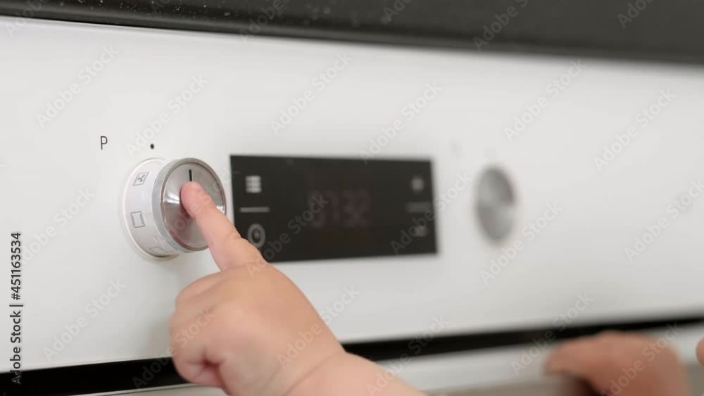 Child pressing oven buttons. Curious little baby opening oven at home in kitchen. Little helper for mom. Safety and protection of children Child pressing oven buttons. Curious little baby opening oven at home in kitchen. Little helper for mom. Safety and protection of children