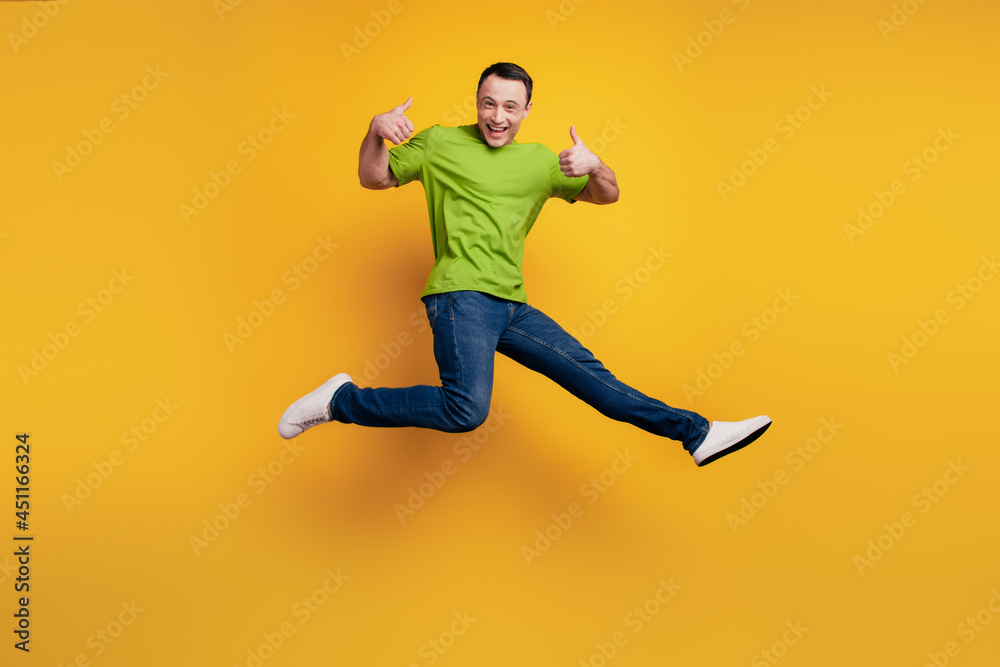 Portrait of funky excited guy jump raise thumb up have fun on yellow wall