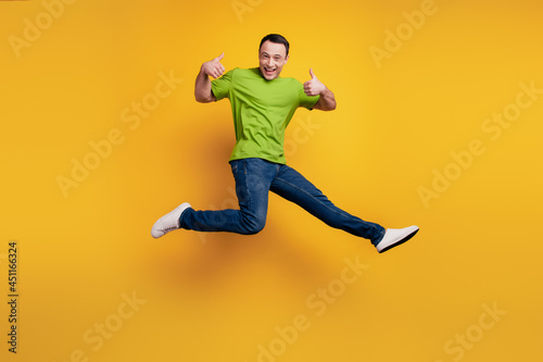 Portrait of funky excited guy jump raise thumb up have fun on yellow wall © Tetiana