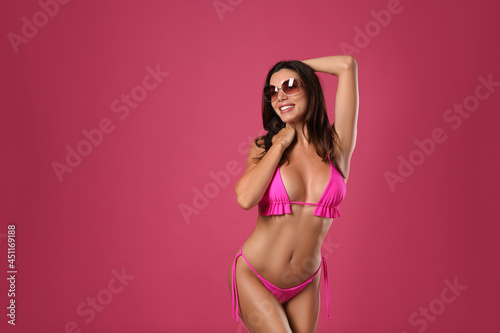 Beautiful woman in stylish bikini and sunglasses on crimson background. Space for text