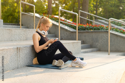Sport and Fitness Young Adult Caucasian Woman Sitting Exercise Mat Concrete Floor Resting after morning Workout Outdoor Summer Park © Andrii