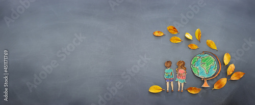 Back to school concept. Top view banner of kids next to globe with autumn dry leaves over classroom blackboard background