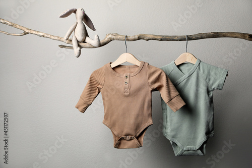 Foto Baby bodysuits and toy on decorative branch near light wall