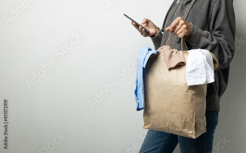 Woman hoding paper pack full of used clothes and using smartphone for searching special recycling bins.Empty space
