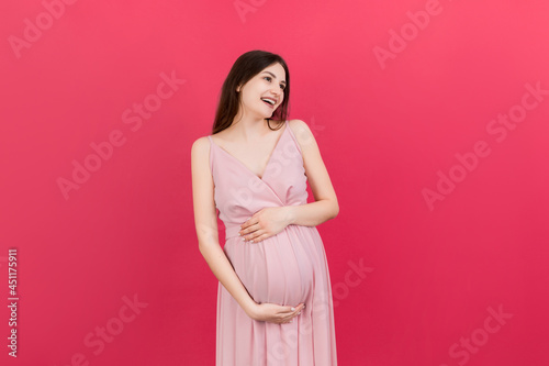 Happy pregnant woman touching her abdomen at Colored background. Future mother. Expecting of a baby. Copy space © sosiukin