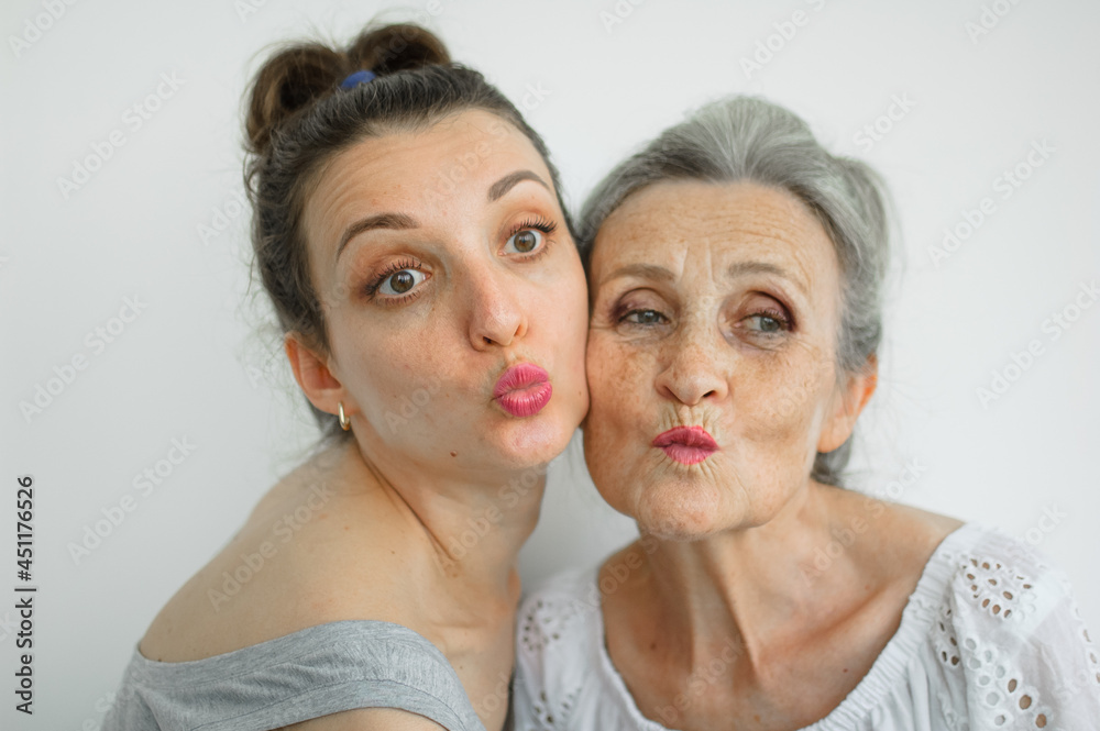 Happy senior mother is hugging her adult daughter, the women are laughing together, sincere family of different age generations having fun on white background, mothers day. Happy senior mother is hugging her adult daughter, the women are laughing together, sincere family of different age generations having fun on white background, mothers day.