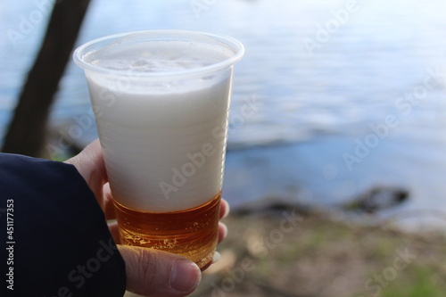 in the hand is a plastic cup with fresh beer on a picnic