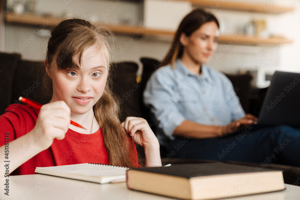 Girl doing homework while her mother working with laptop Girl doing homework while her mother working with laptop