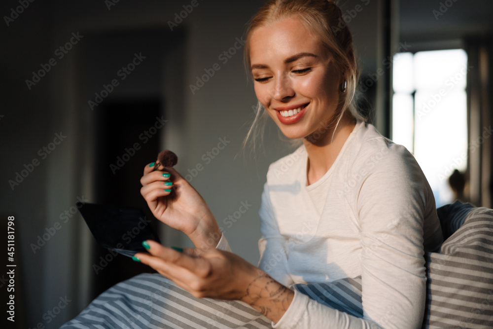 White blonde woman smiling and doing makeup while sitting in bed White blonde woman smiling and doing makeup while sitting in bed