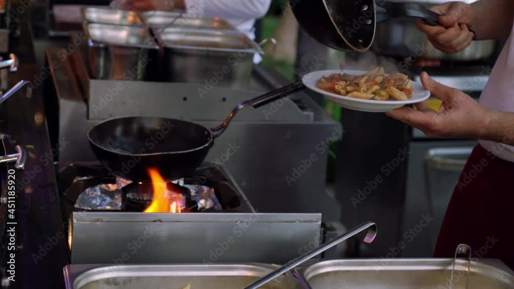 Chef preparing food in an old skillet over a gas burner in a close up on him tossing the food in the pan in a restaurant kitchen Chef preparing food in an old skillet over a gas burner in a close up on him tossing the food in the pan in a restaurant kitchen