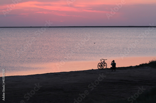 The man next to the bike is filming the sunset near the water