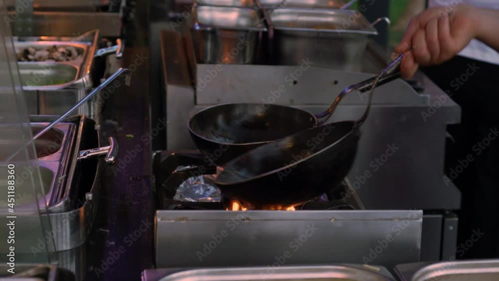 Chef cooking over a gas burner with skillets at an outdoor restaurant in a close up on his hand and the cookware Chef cooking over a gas burner with skillets at an outdoor restaurant in a close up on his hand and the cookware