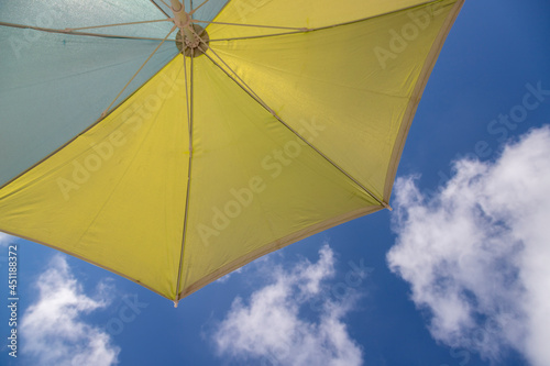 Yellow and blue beach umbrella with blue sky background and white clouds.