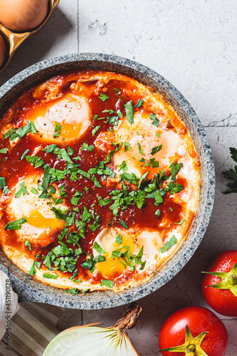 Traditional Israeli shakshuka in gray frying pan. Fried eggs in tomato sauce, close-up.