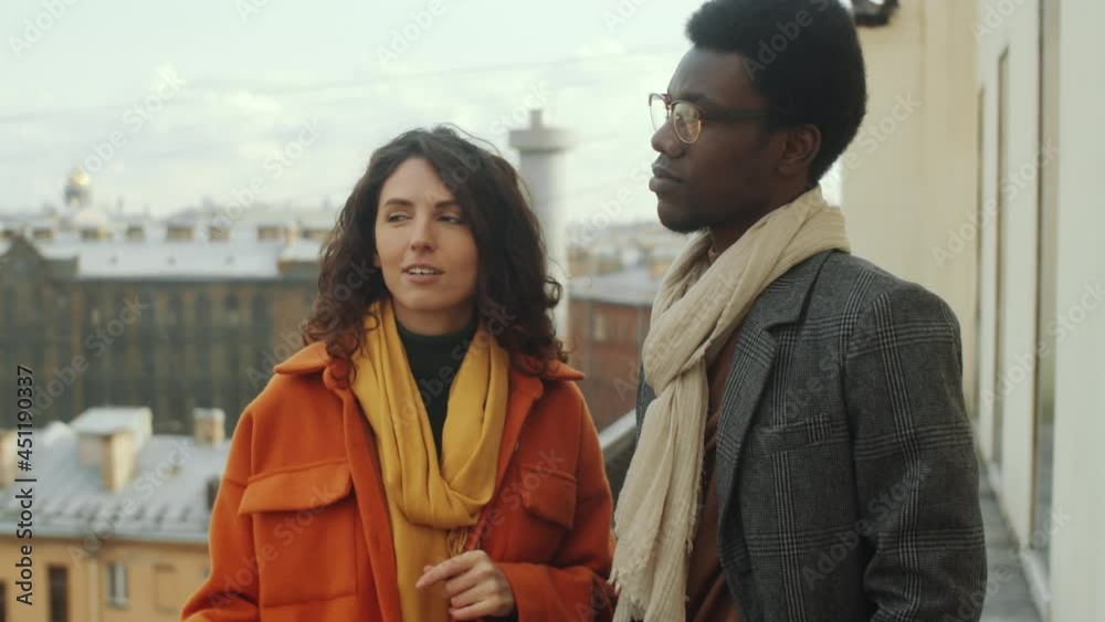 Caucasian woman and Afro-American man standing together on rooftop terrace and having discussion