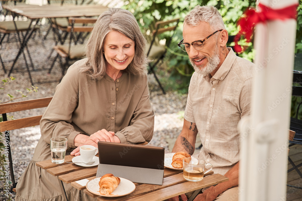 Married woman and man sitting at the cafe and holding tablet while looking at it Married woman and man sitting at the cafe and holding tablet while looking at it
