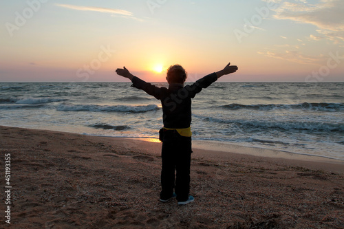 A boy stands with his arms outstretched meets the dawn by the ocean