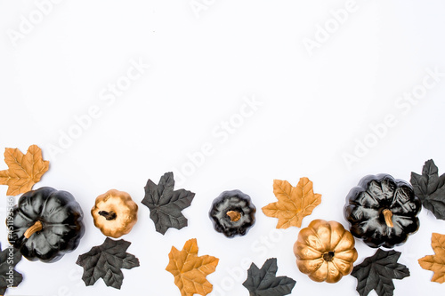Banner. Modern background with autumn leaves and black, golden pumpkins on a white background. Halloween with copy space for text. Flat lay, top.