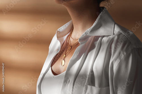 beauty, fashion and jewelry trends concept - close up of woman in white shirt wearing golden multi layer necklace with coin medallions