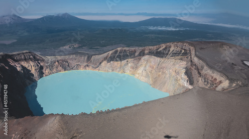 A lifeless acid lake in the caldera of an extinct volcano. Turquoise water with yellow sulfur deposits. Steep rocky slopes. The shadow of a helicopter. View from a height. Kamchatka