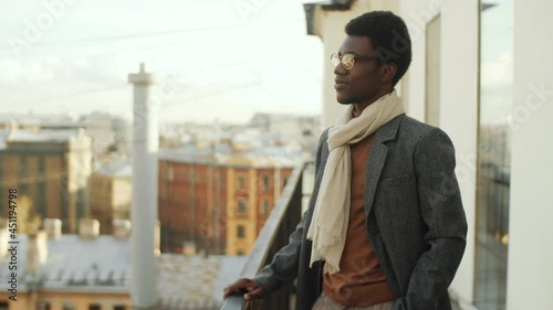 Wallpaper Mural Portrait of stylish Afro-American businessman in coat and scarf standing on rooftop terrace, posing for camera and smiling Torontodigital.ca
