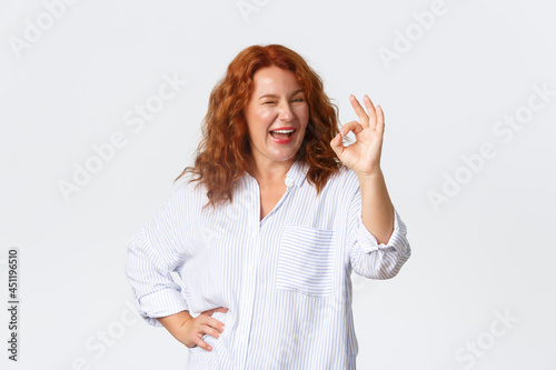 Sassy good-looking middle-aged redhead woman assure everything okay, guarantee or recommend something, approve plan, agree with you, standing pleased over white background photo