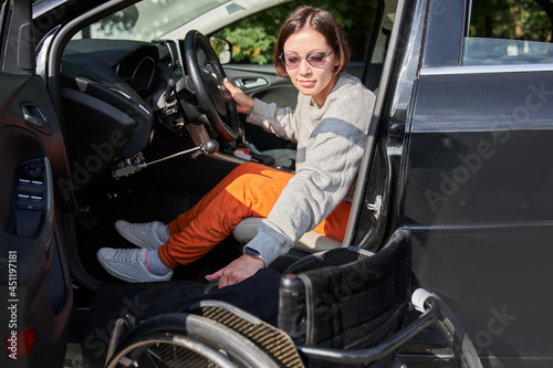 Young disabled person getting out from the wheelchair in her car photo