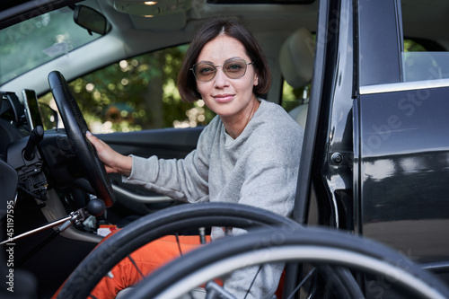 Woman wearing sunglasses folding her wheelchair into the car and smiling to the camera
