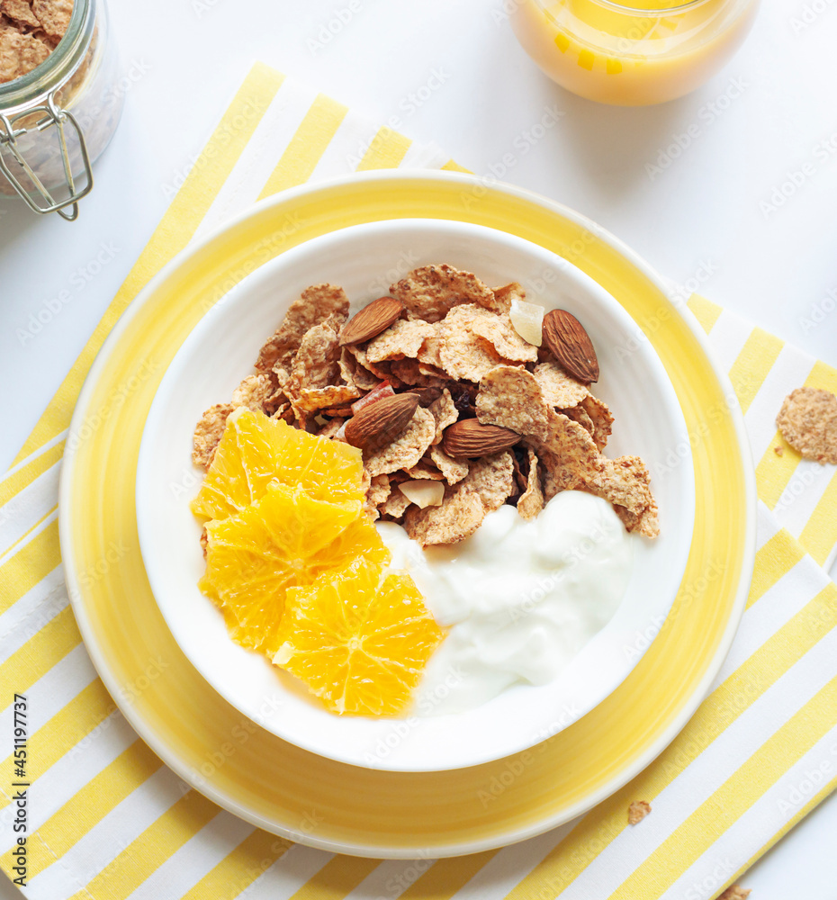 Whole grain oats and wheat flakes with orange, almond nuts and yogurt in a white bowl. Healthy morning breakfast concept close up Whole grain oats and wheat flakes with orange, almond nuts and yogurt in a white bowl. Healthy morning breakfast concept close up