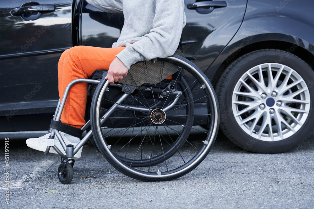 Obraz premium Young girl with lower body disability switches position from the wheelchair into the car