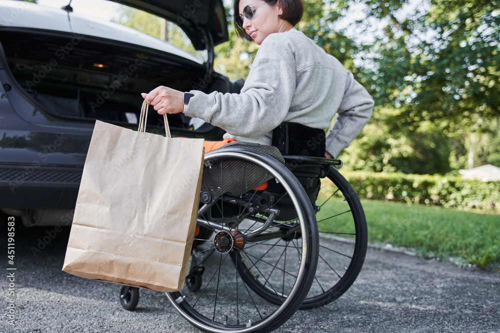 Obraz premium Handicapped woman at the wheelchair holding her purchases and putting shopping bag
