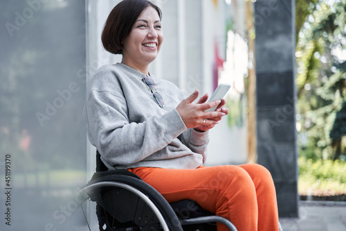 Tableau sur toile Disabled woman holding smartphone and looking away while sitting at the wheelcha