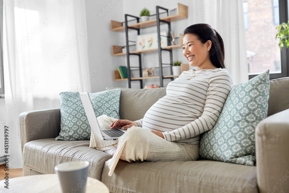 pregnancy, rest, people and expectation concept - happy smiling pregnant asian woman with laptop computer sitting on sofa at home pregnancy, rest, people and expectation concept - happy smiling pregnant asian woman with laptop computer sitting on sofa at home