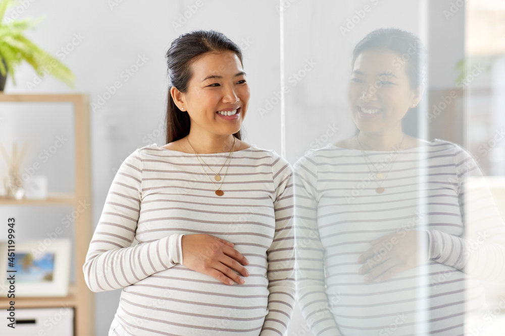 pregnancy, rest, people and expectation concept - happy smiling pregnant asian woman touching her belly at home pregnancy, rest, people and expectation concept - happy smiling pregnant asian woman touching her belly at home